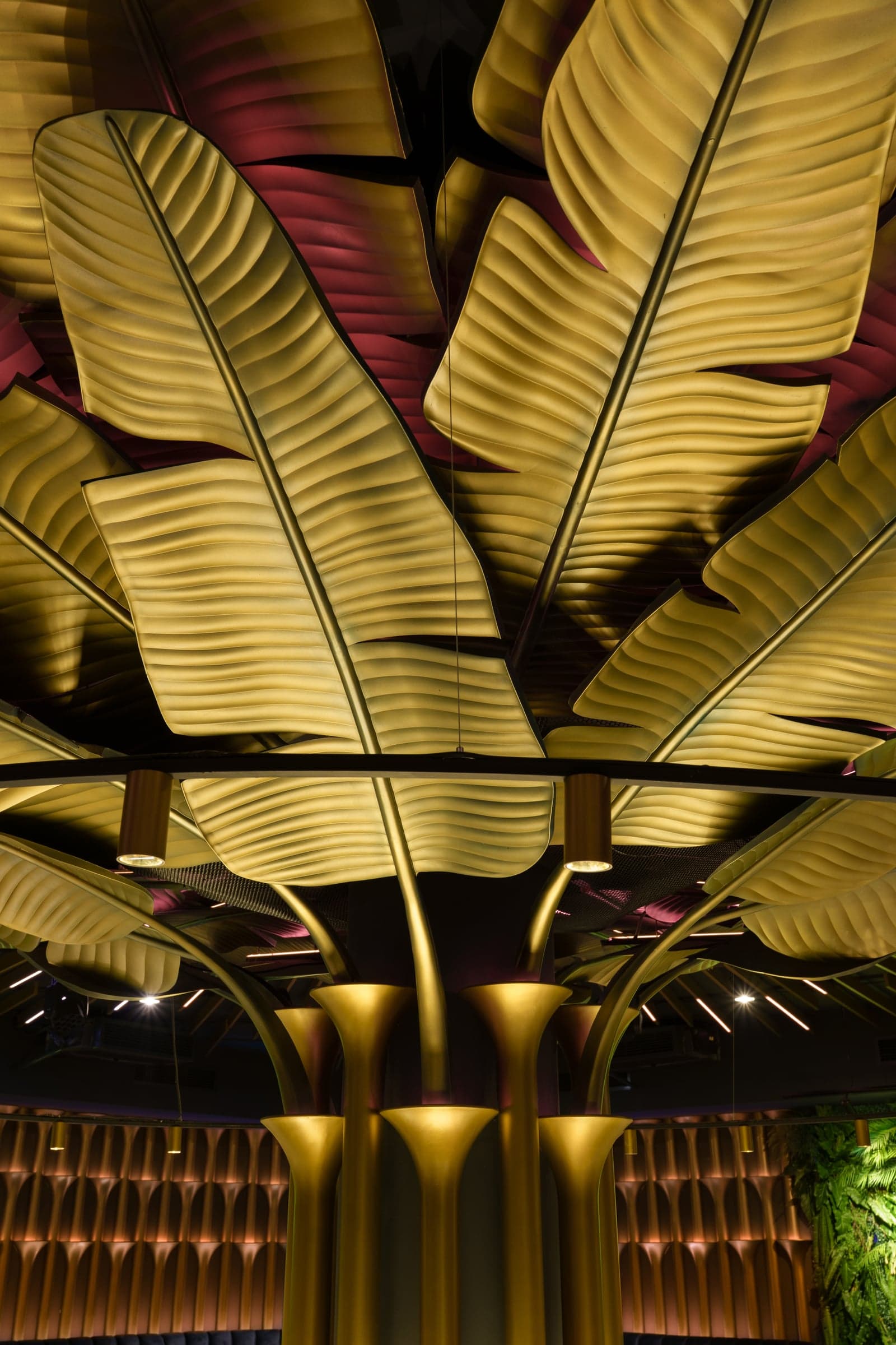 Sculptural gold banana-leaf ceiling installation over a hospitality dining room