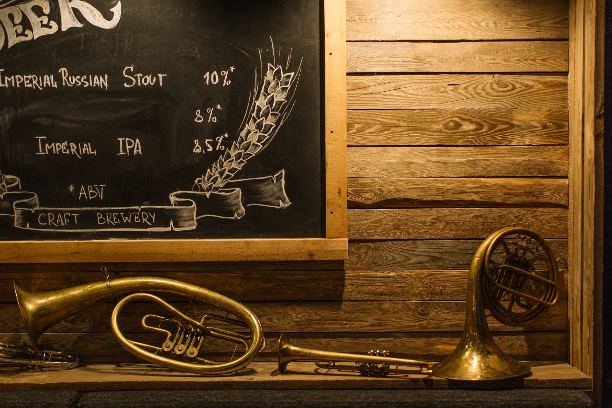 Hand-chalked brewery menu board beside vintage brass instruments on a timber wall